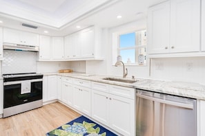 A kitchen with white cabinetry, a built-in oven, a dishwasher, and a window with a view. - Oceanfront & River View 3BD/2BA @ Grand Coquina 501 (Daytona Beach Shores)