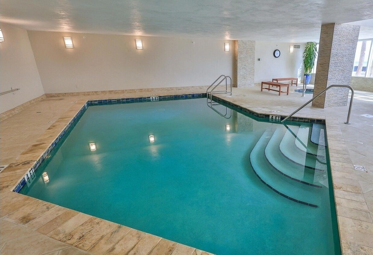 Une piscine intérieure à l’eau claire, dotée d’un sol carrelé et de quelques marches menant à l’eau.