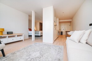 Una habitación moderna y bien iluminada, con un sofá blanco, un escritorio de madera y una alfombra estampada.