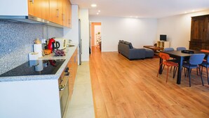 Uma cozinha moderna com armários de madeira, bancada de granito e um espaço de refeições com sofá cinza e televisão.