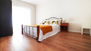 Quarto com uma cama, mesa de cabeceira e janela com cortinas.