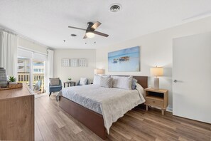 Een slaapkamer met een bed, nachtkastjes, een plafondventilator, een schilderij en uitzicht op een balkon.