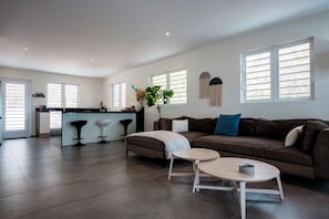 Ein geräumiger Wohnbereich mit braunem Sofa, einem Couchtisch und einer Küchenzeile mit Barhocker.