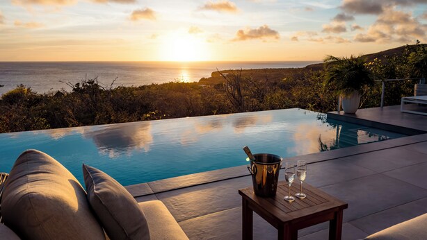 A poolside view with a sunset, a table with a bucket and glasses, and a sofa. - Aqua Vista, Oceanview Villa with infinity pool Coral Estate close to the beach! (Sint Willibrordus)