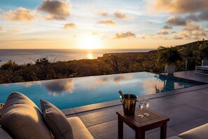 A poolside view with a sunset, a table with a bucket and glasses, and a sofa. - Aqua Vista, Oceanview Villa with infinity pool Coral Estate close to the beach! (Sint Willibrordus)