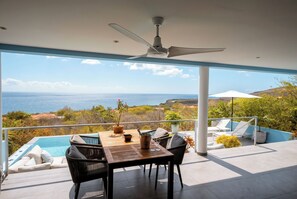 A balcony with a pool, a table, chairs, and a ceiling fan. - Aqua Vista, Oceanview Villa with infinity pool Coral Estate close to the beach! (Sint Willibrordus)