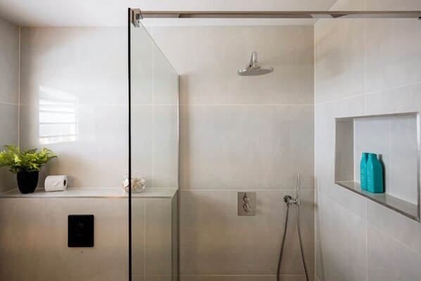 A modern shower with a glass door, a potted plant, a toilet paper roll, and a shelf with toiletries.
