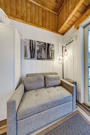 A modern living room with a grey sofa, wooden ceiling, and wall-mounted artwork.