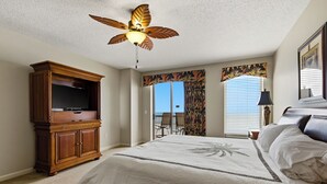 Ein Schlafzimmer mit einem Bett, einem Deckenventilator, einem Fernseher, einem Fenster mit Vorhängen und Blick ins Freie.