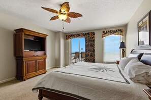 A bedroom with a bed, a ceiling fan, a television, a window with curtains, and a view of the outdoors. - Margate Towers 1403 - Ocean views from Private Deck! (Myrtle Beach)