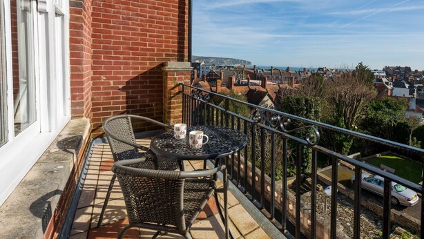 Uma varanda com mesa e cadeiras, vista para a cidade e um muro de tijolos.