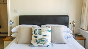 Uma cama com cabeceira escura, duas mesas de cabeceira com abajures e uma obra de arte na parede.