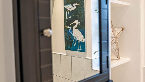 A framed artwork with two birds on a wall, a door, and a shelf with decorative items.