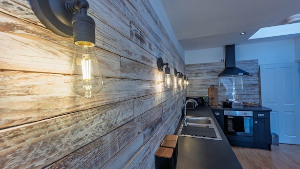 A modern kitchen with wooden wall paneling, a built-in oven, and a countertop with a sink. - 3 The Yard (Swanage)