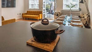 A modern kitchen with a large stove, wooden cutting board, and a dining area with a sofa and chairs. - 3 The Yard (Swanage)