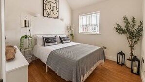A bedroom with a bed, bedside tables, a window, and a plant. - 3 The Yard (Swanage)