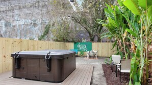 Uma banheira de hidromassagem em um deck de madeira, cerca de madeira e uma placa com 'Welcome to Nola' ao fundo.