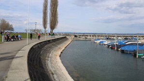 Eine Uferpromenade mit einer gewundenen Böschung, eine Reihe von Booten, die an der rechten Seite festgemacht sind, und Menschen, die den Weg entlanggehen.