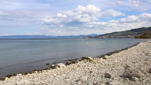 Eine felsige Küstenlinie mit ruhigem Wasser, entfernten Bergen und wolkenlosem Himmel.