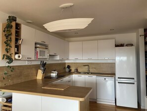 A modern kitchen with white cabinets, a wooden island, a built-in microwave, a sink, and a white refrigerator. - 200m from the sea: Recent 2-person apartment with terrace and unobstructed view (Pleumeur-Bodou)