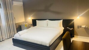 A hotel room with a large bed, a nightstand, a desk, and a chair. - SNL Mountain View Hotel (Akosombo)
