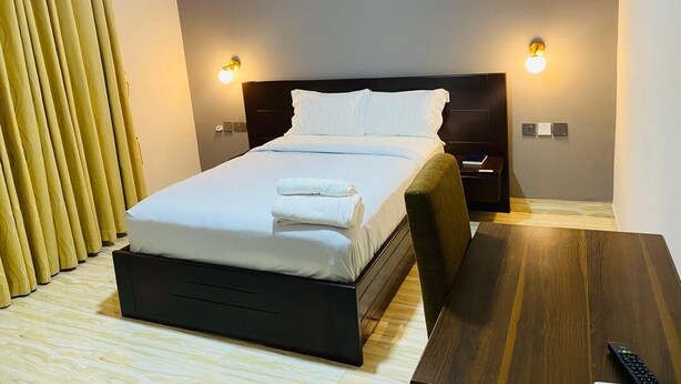 A hotel room with a bed, bedside tables, a wooden floor, and curtains. - SNL Mountain View Hotel (Akosombo)