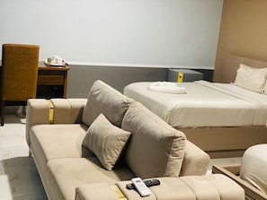 Una habitación de hotel con sofá, cama, mesita de noche y una silla.