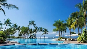 Ein Poolbereich mit mehreren Schwimmbecken, Palmen und Liegestühlen.