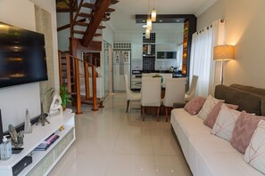 A modern living room with a sofa, TV, and a staircase leading to a kitchen. - Casa c Churrasqueira a 350m da Praia de Massaguaçu (Caraguatatuba)