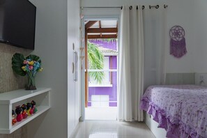 A bedroom with a bed, a TV, a shelf with figurines, and a view of a purple building. - Casa c Churrasqueira a 350m da Praia de Massaguaçu (Caraguatatuba)