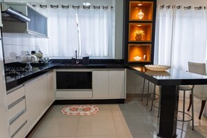 A modern kitchen with a stove, sink, and a dining area with a table and chairs. - Casa c Churrasqueira a 350m da Praia de Massaguaçu (Caraguatatuba)