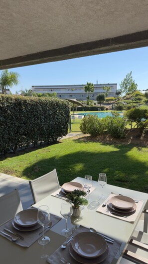 Ein Esstisch draußen mit Blick auf einen Pool und Gebäude im Hintergrund.