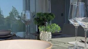 Une table à manger avec des assiettes, des verres et des couverts, une petite plante en pot et une fenêtre avec des rideaux.
