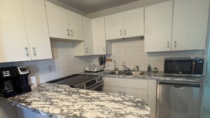 Een keuken met witte kasten, een roestvrijstalen vaatwasser, een magnetron en een granieten aanrechtblad met bar.