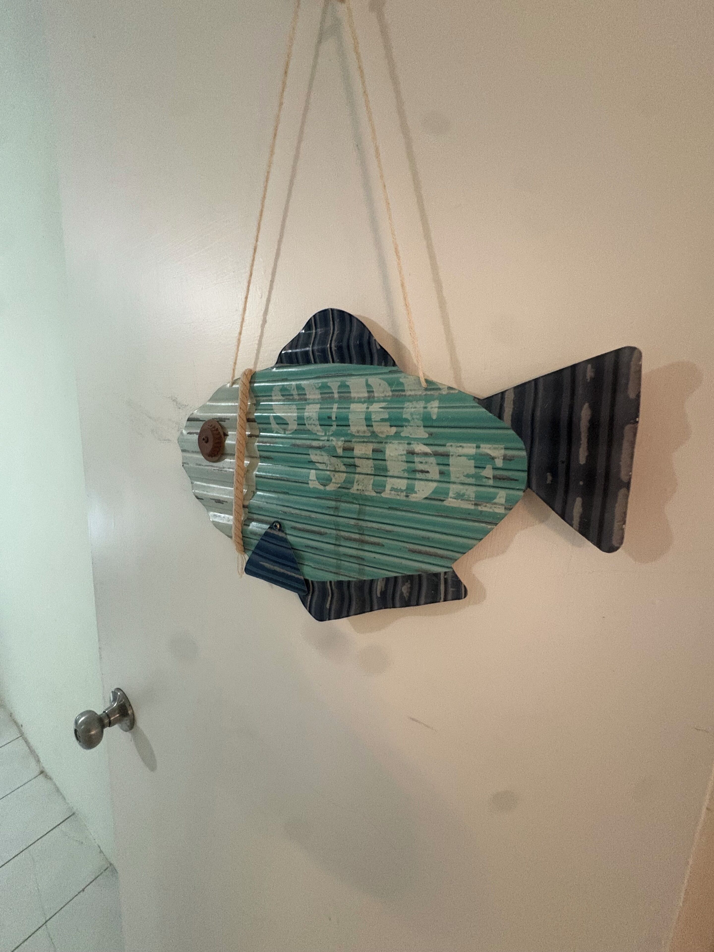 Een visvormige decoratie aan de muur, met de tekst 'SURE SIDE' en een deurklink links.