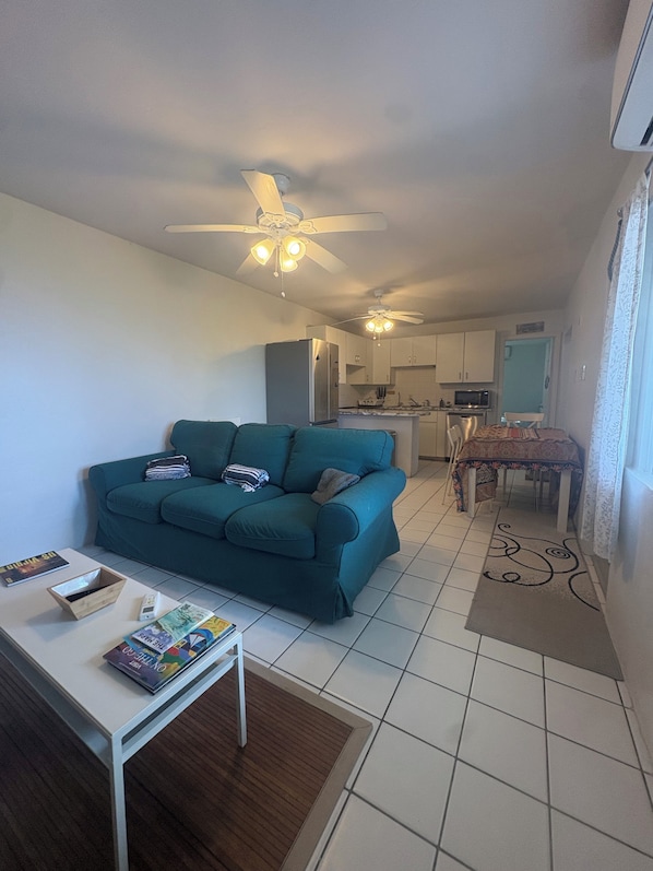 A compact living space with a sofa, a small table, a kitchenette, and a ceiling fan.