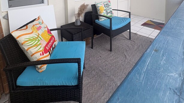 Een kamer met twee rieten stoelen met blauwe kussens, een bijzettafeltje met een vaas, en een deur met een sleutelgat.
