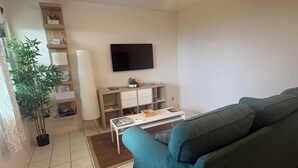 Een woonkamer met een groene bank, een flatscreen televisie aan de muur, een plafondventilator en een kleine tafel met een afstandsbediening.