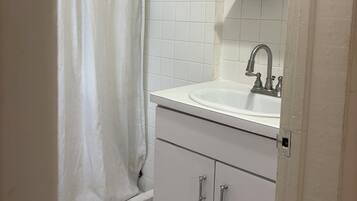 A bathroom with a shower curtain, a sink, a mirror, and a cabinet.