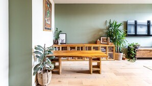 Um banco de madeira num espaço com parede verde, uma televisão e diversos vasos de plantas.