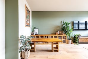 Eine hölzerne Bank in einem Raum mit grüner Wand, einem Fernseher und mehreren Blumentöpfen.