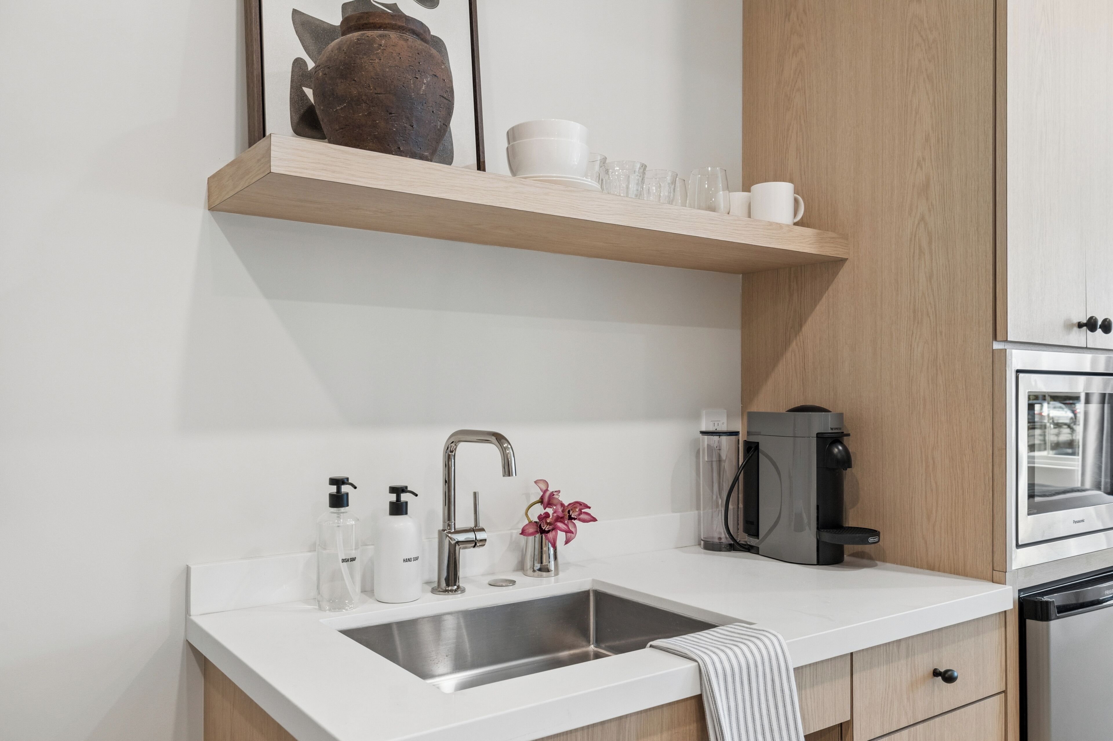 Una cocina moderna con un lavamanos de acero inoxidable, una cafetera y un horno empotrado.