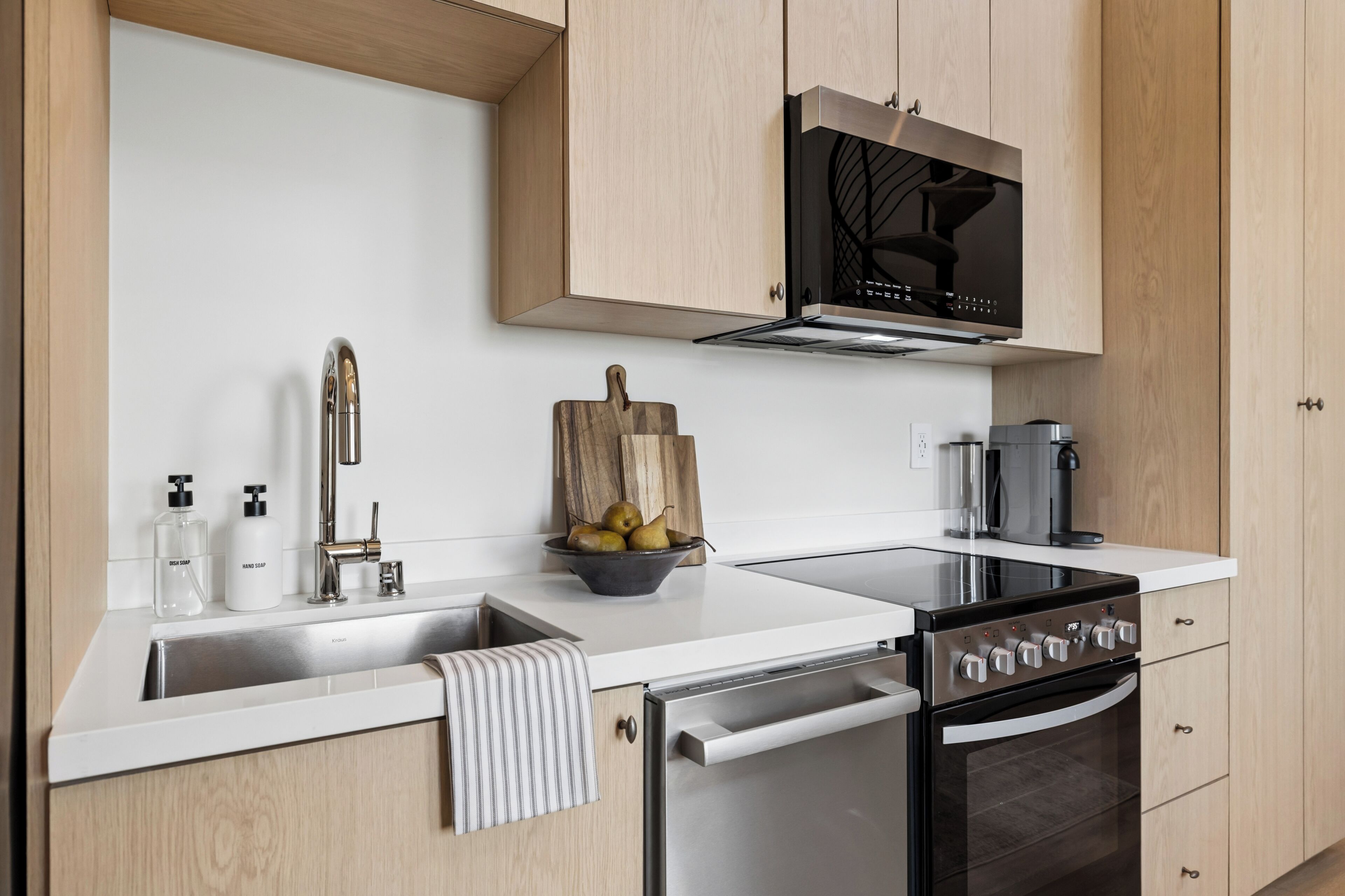 A modern kitchen with a stainless steel sink, a built-in oven, a microwave, and wooden cabinets.