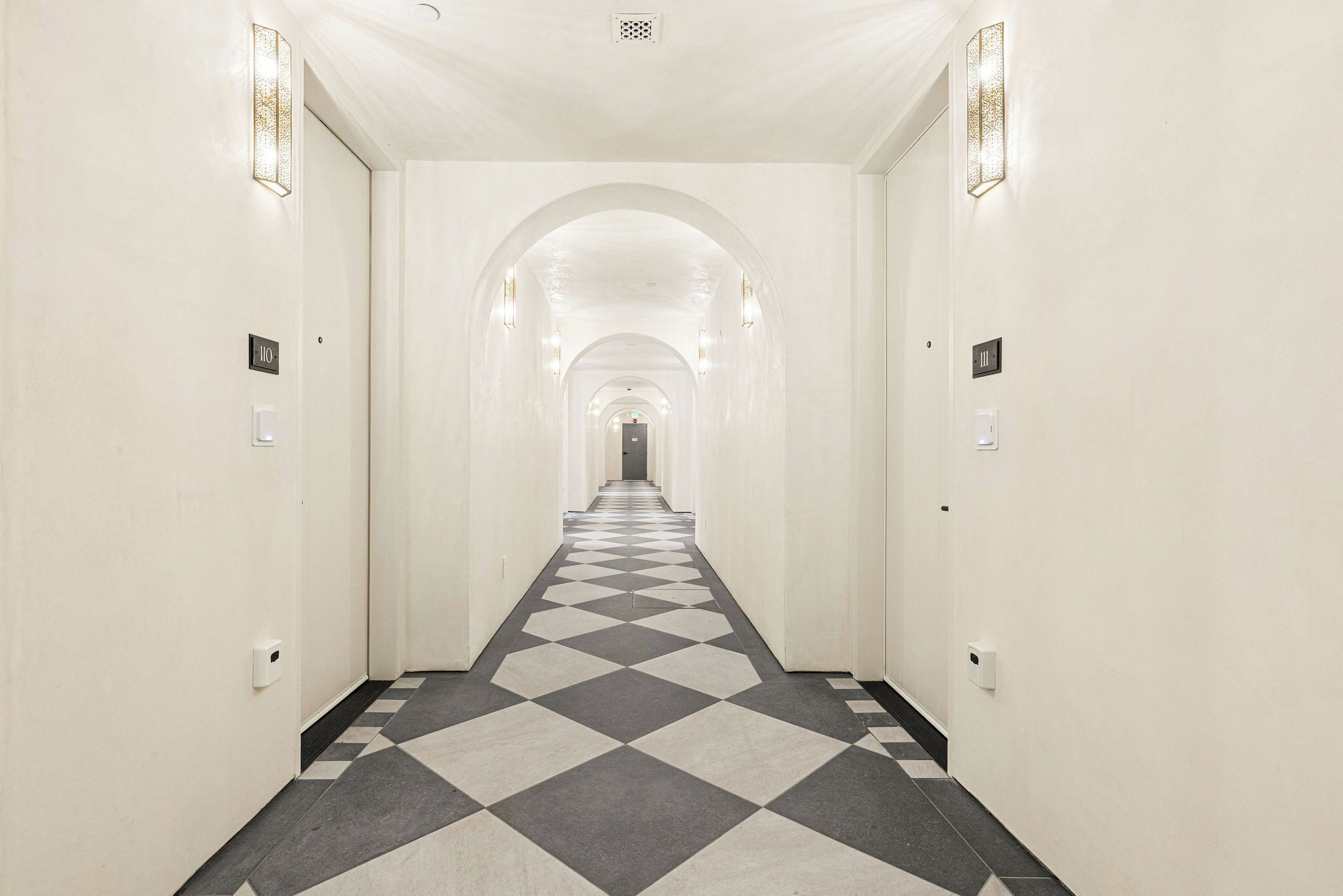 A hotel hallway with a checkered floor, white walls, and arched doorways.