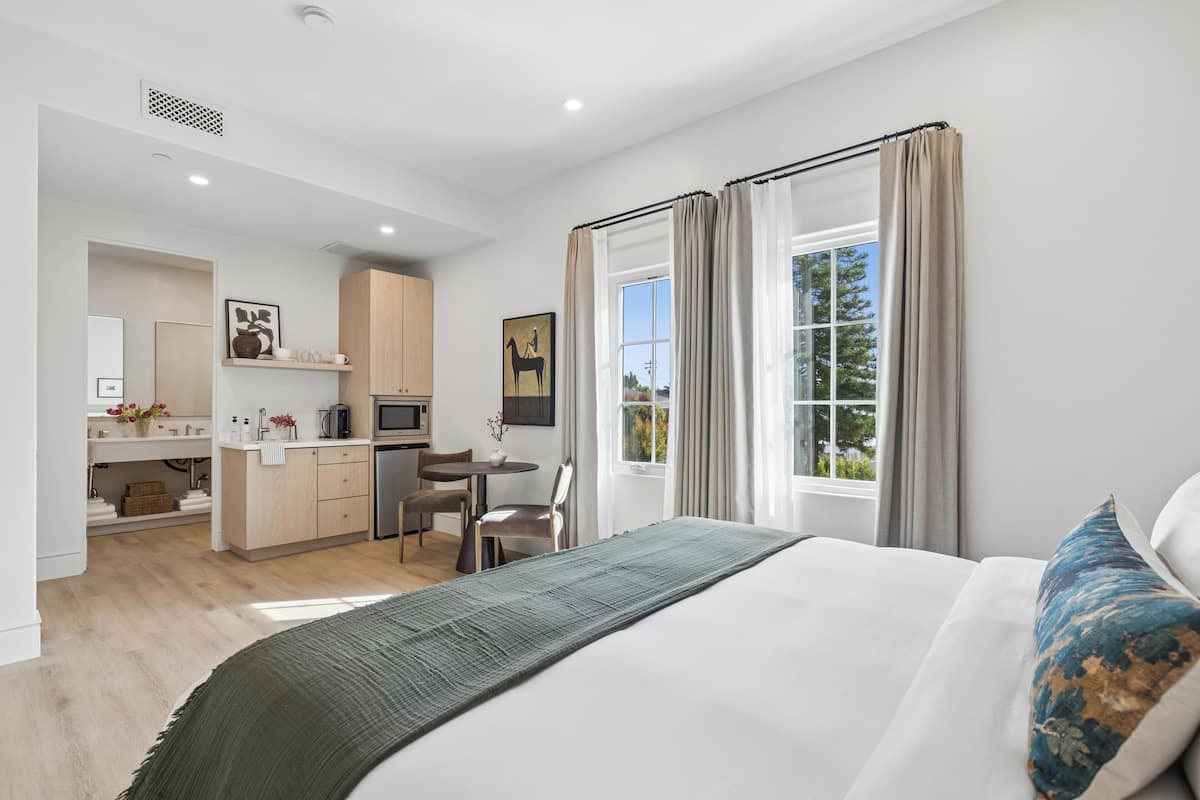 Moderni hotellihuone, jossa on sänky, työpöytä ja pieni keittiö.