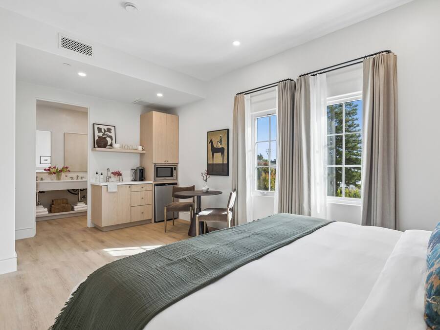 A modern hotel room with a bed, a desk, and a kitchenette.