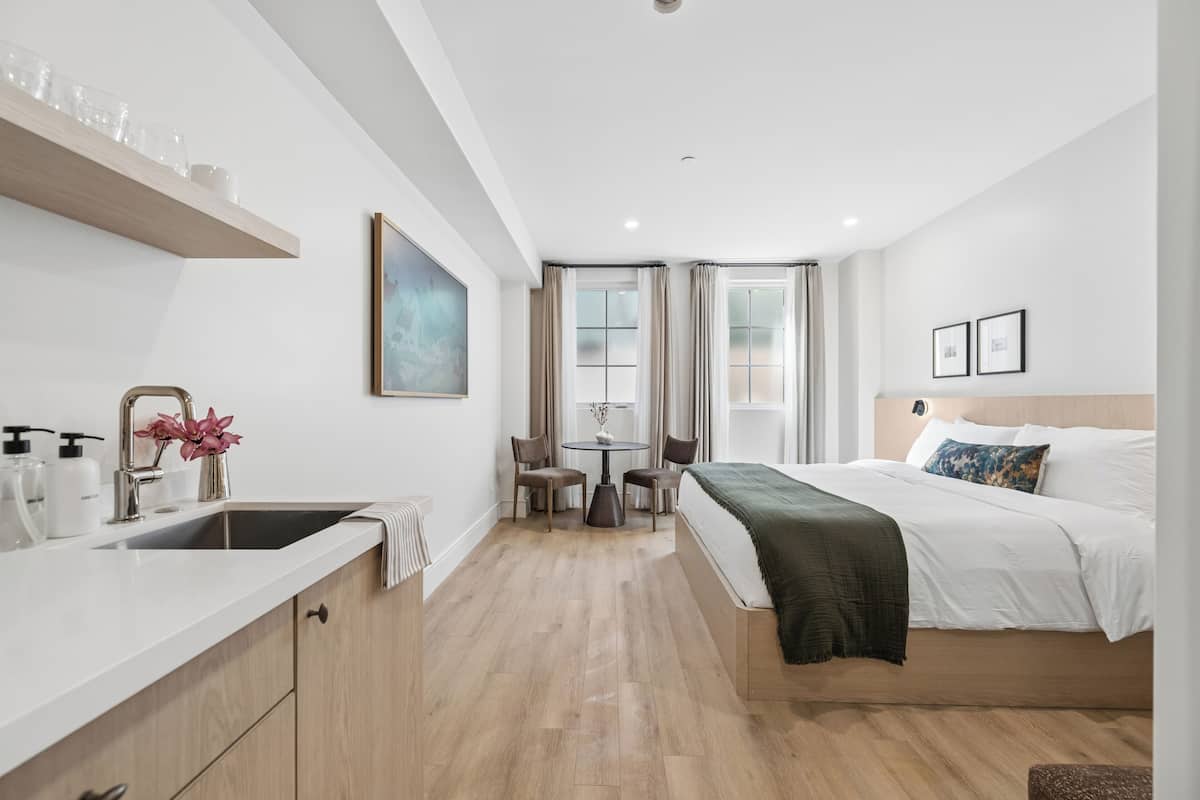 Moderni hotellihuone, jossa on sänky, yöpöytä ja pieni keittopiste.