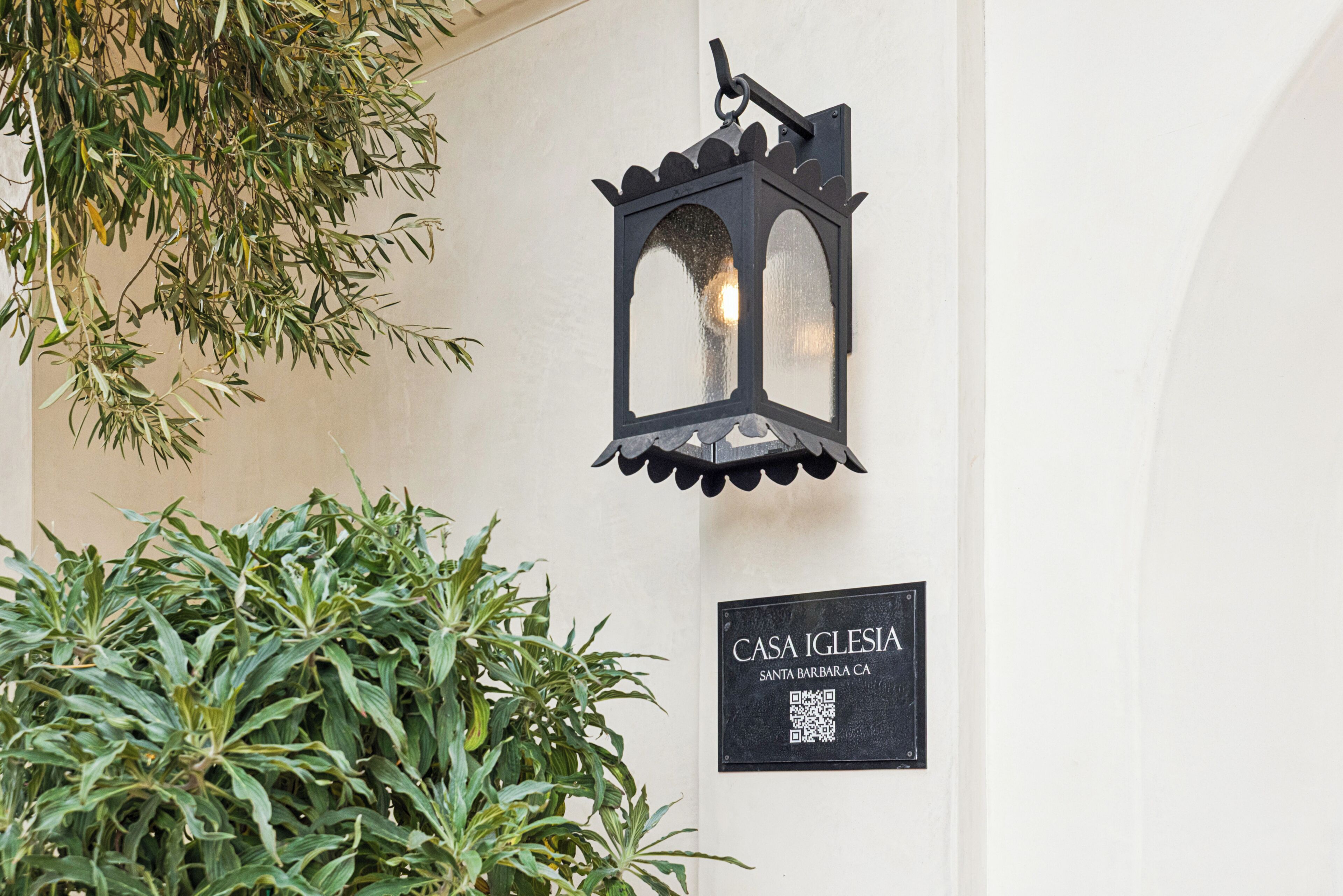A wall-mounted lantern, a sign reading 'CASA IGLESIA SANTA BARBARA CA', and a potted plant.