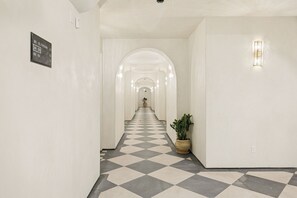 Un couloir d'hôtel avec un sol à carreaux, des murs blancs et une plante en pot.
