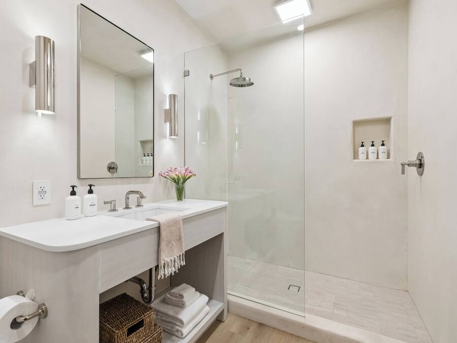 A modern bathroom with two sinks, a large mirror, a glass shower enclosure, and a small shelf with toiletries.